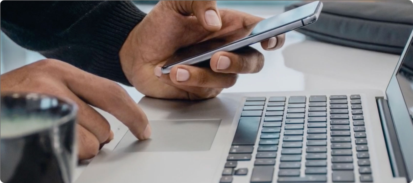Person holding a smart phone with their left hand and using their right index finger on a laptop trackpad.