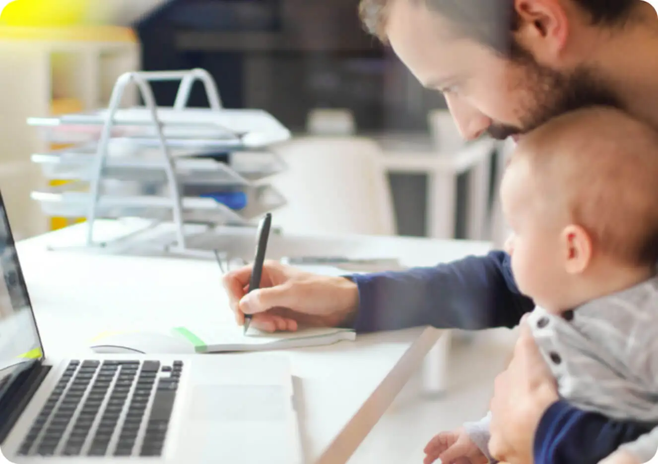 A man holding a baby and writing on a desk.