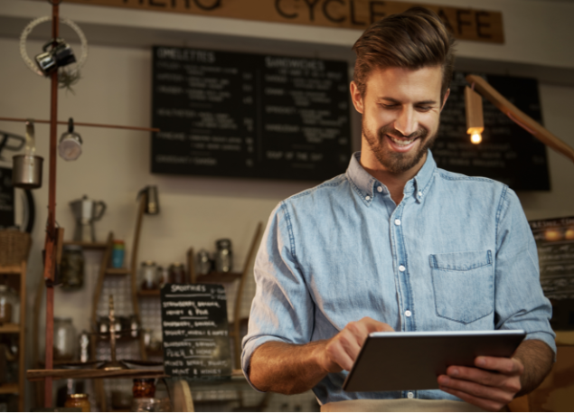 Man in a coffee shop smiling and working on a tablet.