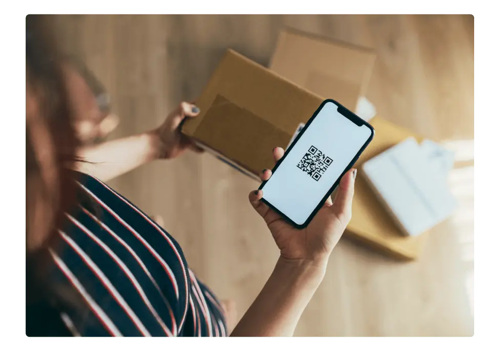 Person looking at mobile device with a QR code displayed, and holding a package.